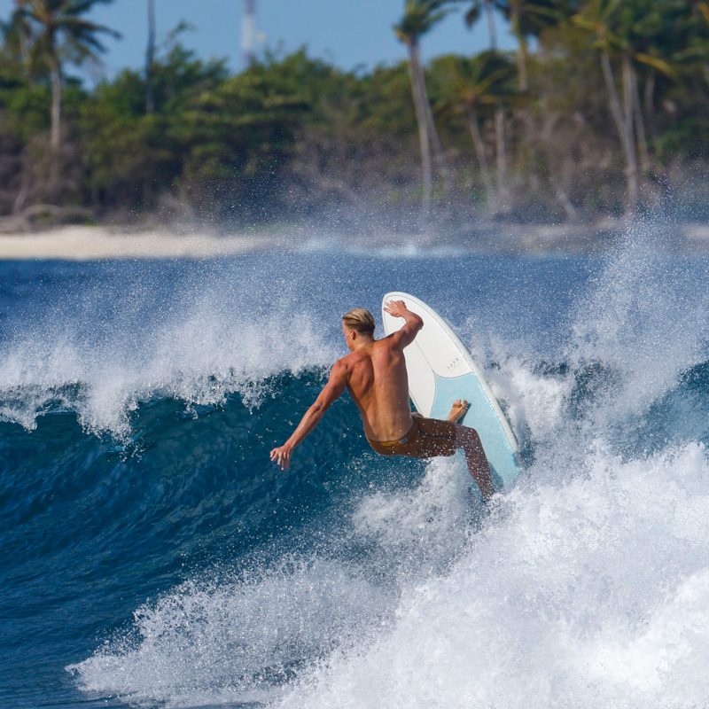 Surfer riding a wave on a white surfboard near a tropical beach, Melbourne Surfboard Shop
