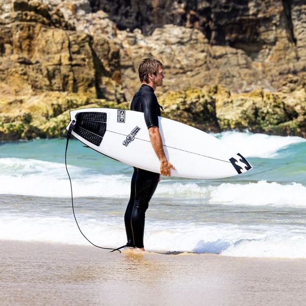 A male surfer in a wetsuit on the edge of the ocean and beach,  holding a JS Industries surfboard under his arm.  Purchased from Melbourne Surfboard Shop 