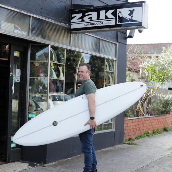 Fathers day gift guide for the surfing dad in your family.  Man looking at the surfboard his family bought him for fathers day, with a surf beach as his vista.