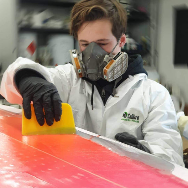 Applying a flow of resin to a surfboard using a common glassing tool, the squeegee