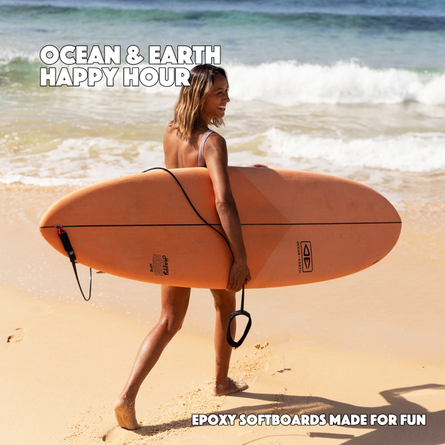 Ocean and Earth Happy Hour - Epoxy Softboard carried on the beach by a woman about to surf.