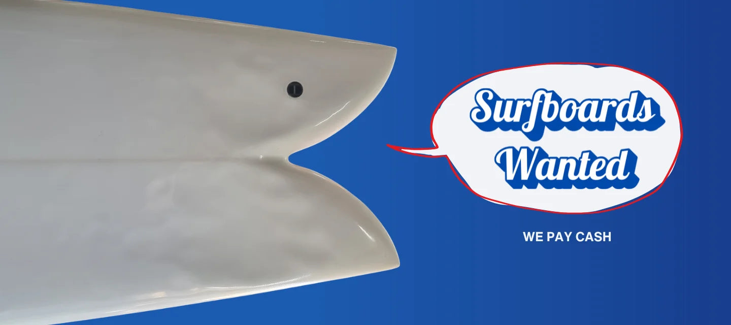 White surfboard with a twin fin design on a blue background, featuring a Surfboards Wanted sign.