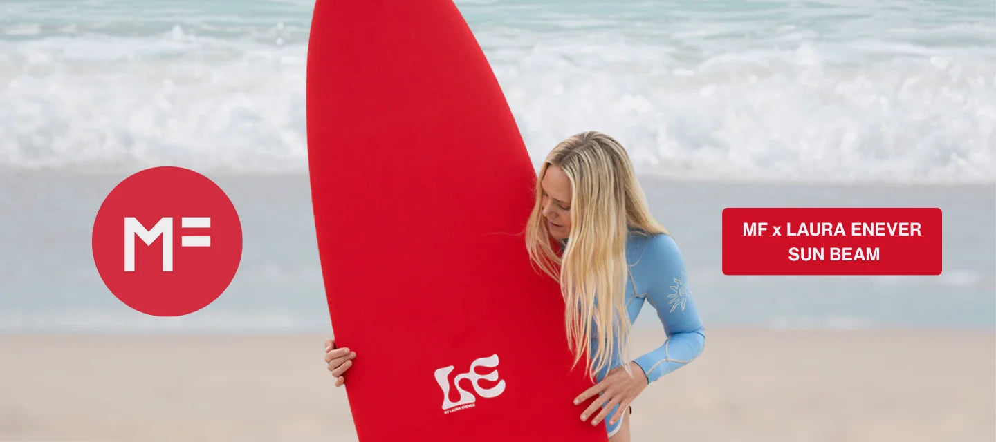 Woman holding a red surfboard with MF and Laura Enever branding on a beach.